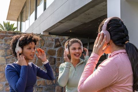 Multiracial women testing and comparing wireless headphones outside modern home