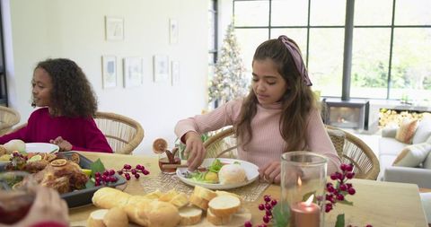 Girls preparing holiday dinner at festive family table with roasted chicken and candles