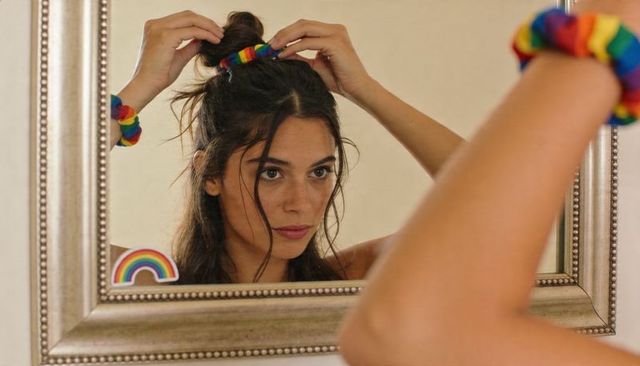 Adjusting hair with rainbow scrunchie at mirror, intimate self-grooming portrait of woman