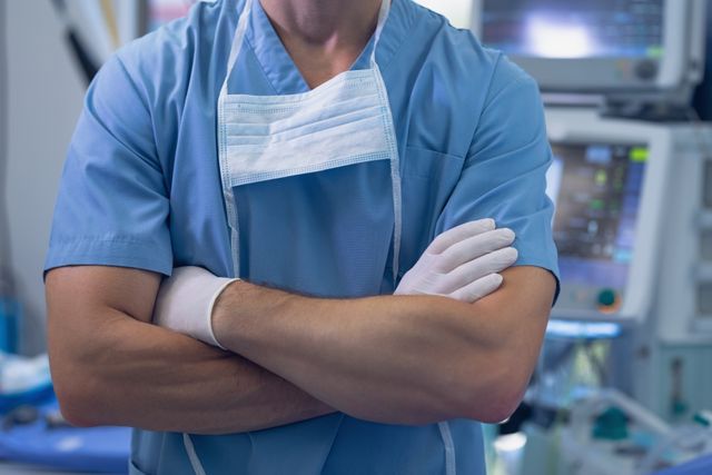Mid section of male surgeon standing with arms crossed in operating room at hospital