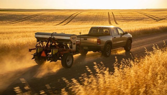 Driving silver pickup towing multi-row planter down dusty country road at golden sunset