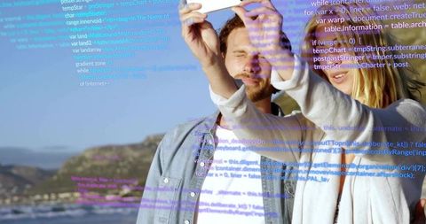 Couple capturing seaside selfie with tablet and digital code overlay