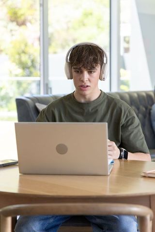 Teenager wearing headphones studying on laptop at home for remote learning