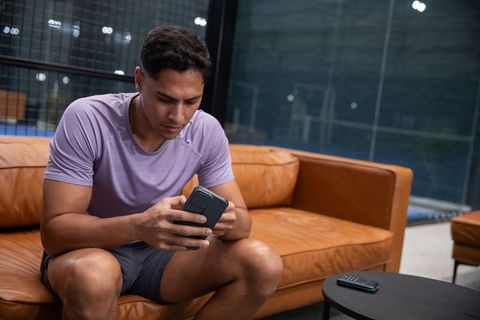 Athlete relaxing on leather sofa checking smartphone in modern indoor sports lounge