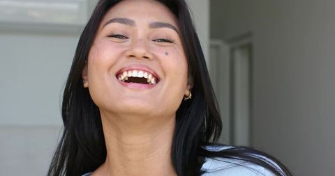 Mid-adult asian woman laughing with bright open smile and gold hoop earrings, candid portrait