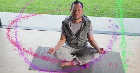 Asian man meditating on backyard deck with magenta and green energy swirls for wellness