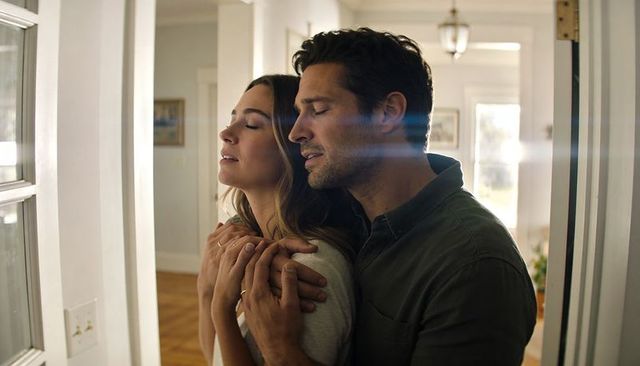 Sunlit couple embracing in foyer by glass door, intimate romantic moment at home