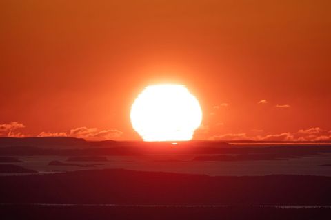 Fiery Sun Dropping Behind Island Horizon Over Calm Sea at Sunset