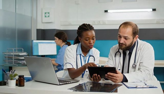 Doctor and nurse reviewing patient records on tablet during clinical team consultation