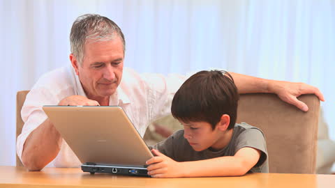 Happy Grandfather Bonding with Curious Grandson Using Laptop