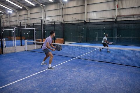 Indoor padel match with two male players returning volley at net on blue court
