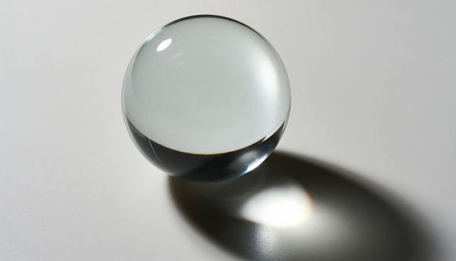 Clear glass sphere casting elongated shadow and caustic highlight on white background
