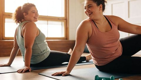 Stretching plus-size women smiling together in sunlit studio for fitness and wellness