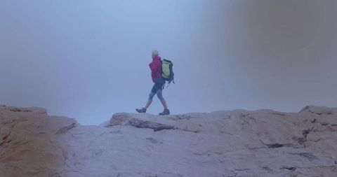 Senior Hiker Walking on Rocky Ridge in Foggy Landscape