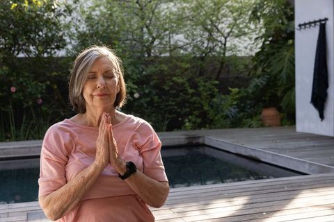 Senior Woman Practicing Meditation by Tranquil Pool