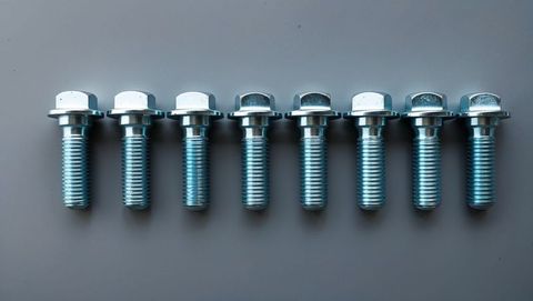 Row of metallic hex flange bolts on smooth grey tabletop