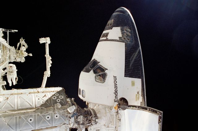 Astronaut conducts spacewalk during STS-113 mission as Space Shuttle Endeavour is docked to the International Space Station. The photograph features the forward section of the shuttle and the Canadarm2 robotic arm. Ideal for use in articles about space exploration, NASA missions, and the construction of the ISS.