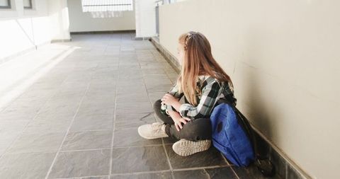 Young Girl in School Corridor Contemplating by Backpack