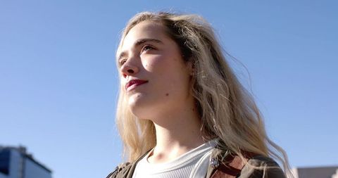 Sunlit woman gazing upward on rooftop, confident portrait for lifestyle and editorial