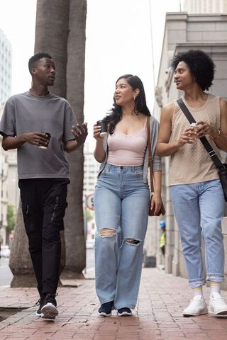 Diverse friends walking and chatting on downtown brick sidewalk holding coffee cups