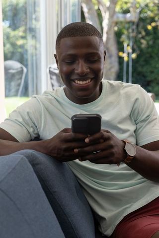 Man smiling while checking smartphone relaxing on sofa