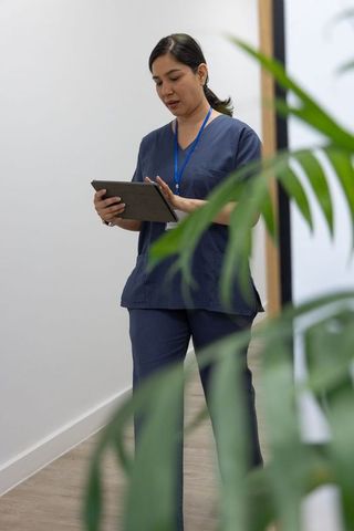Nurse using tablet and checking electronic records in clinic corridor wearing navy scrubs