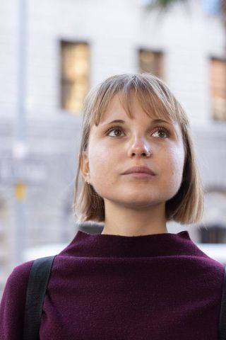 Young woman looking upward on city street wearing maroon sweater and nose hoop