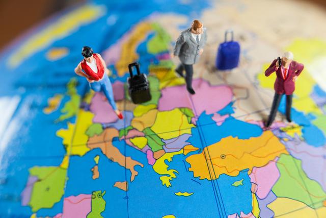 Miniature figurines standing on a colorful world map, symbolizing travel and exploration. Each figure has luggage, representing a journey or adventure. Ideal for use in travel agency promotions, tourist advertisements, globetrotting articles, and educational materials on geography.
