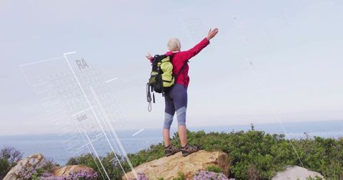 Senior hiker celebrating summit with arms raised overlooking ocean cliffs and purple blooms