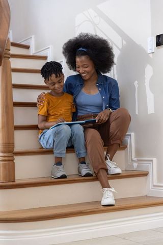 Parent and child reading tablet on wooden stairs, family bonding and learning at home