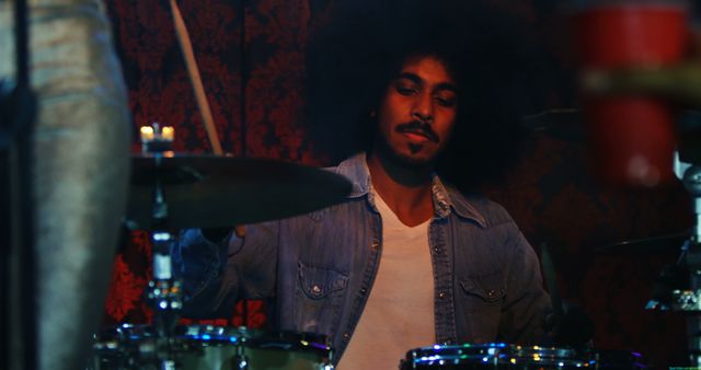 A young African American male musician plays the drums passionately, with copy space. His focus and the vibrant stage lighting create an energetic atmosphere for a live music performance.