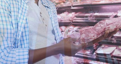 Man holding and examining wrapped beef tray in supermarket meat case while shopping