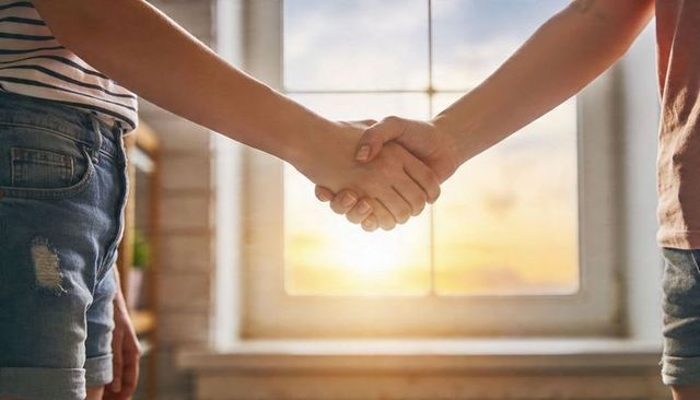 Shaking hands in sunlit room wearing denim shorts and striped top, casual connection