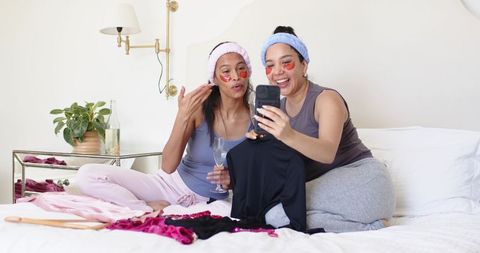 Multicultural friends enjoying pamper night in loungewear with under-eye patches and wine
