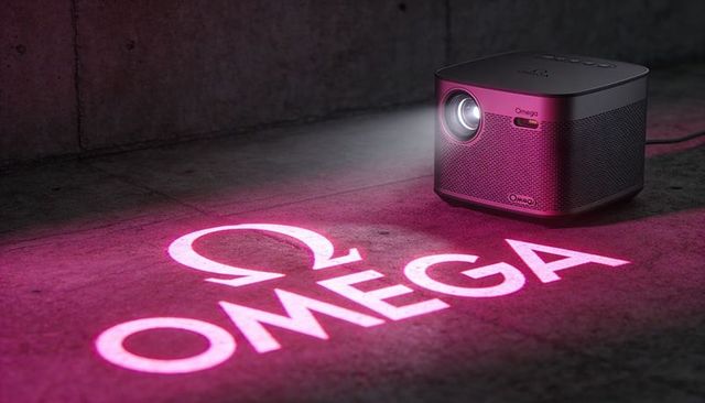 Compact cube projector projecting magenta omega logo and symbol onto urban concrete floor