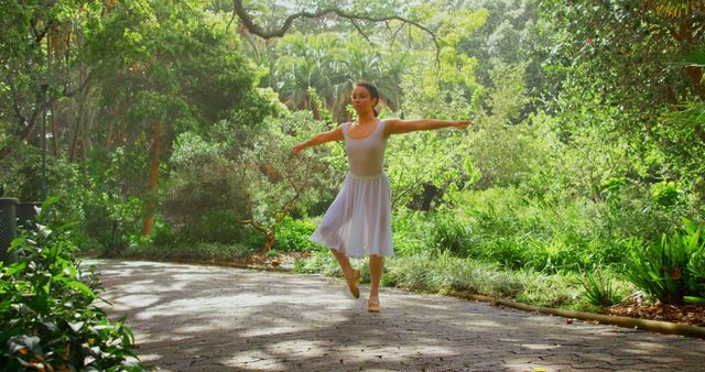 Woman is dancing ballet on a sunlit path surrounded by lush greenery in a forest park. This image conveys tranquility, elegance, and the beauty of nature. Perfect for websites, blogs, or advertisements focused on dance, nature retreats, and wellness.