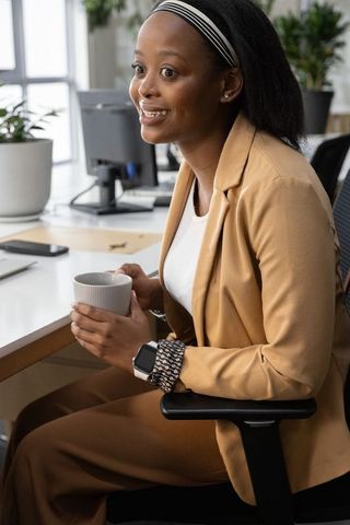 African american professional smiling at desk holding coffee mug in modern office