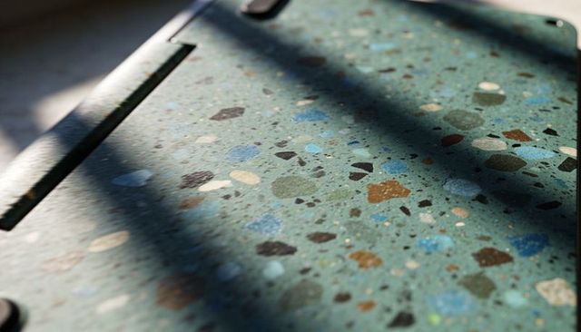 Closeup teal terrazzo tabletop showing multicolor aggregate and diagonal window-shadow