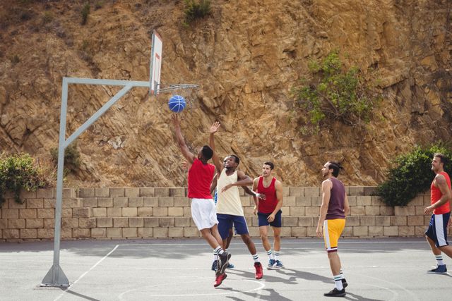 Group of friends playing an intense game of basketball on an outdoor court. Perfect for illustrating themes of sports, teamwork, fitness, and outdoor activities. Ideal for use in articles, advertisements, and social media posts promoting healthy lifestyles and recreational sports.