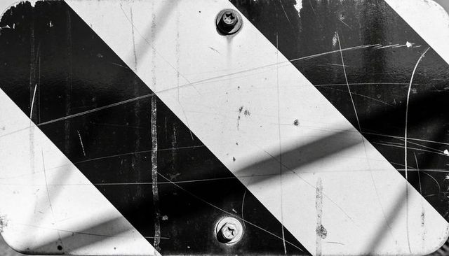 Grungy black and white diagonal hazard stripes on weathered metal panel with bolts