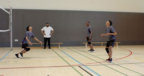 Diverse male volleyball team practicing dynamic passing drill, lunging on indoor gym court