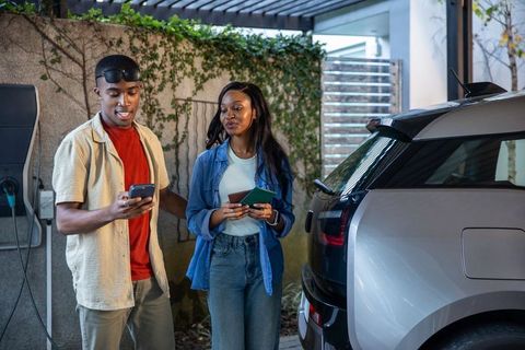 Friends checking smartphone at electric car charging station