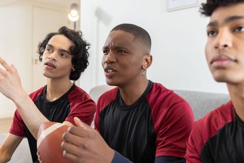 Diverse teen teammates watching game wearing matching jerseys holding football