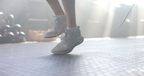 Person Jumping in White Sneakers in Sunlit Gym