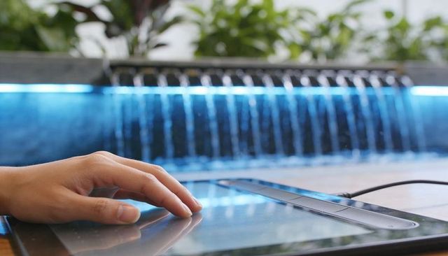 Hand touching graphic tablet on outdoor terrace with blue water curtain and reflection
