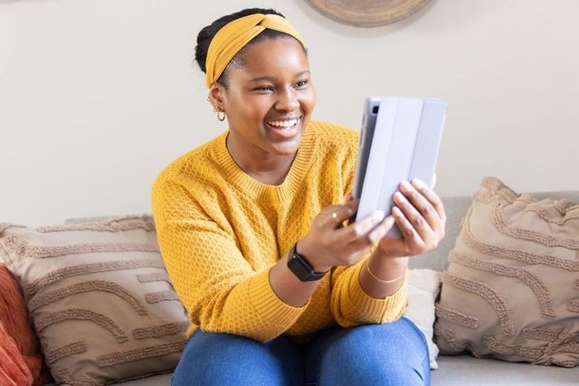 Smiling african american teen holding tablet on cozy sofa, casual home technology