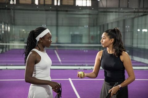 Diverse female tennis players training, discussing tactics on vibrant purple indoor court