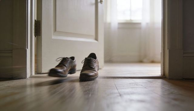 Sunlit brown leather dress shoes resting at doorway on worn hardwood floor