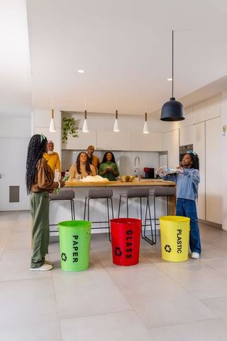 African american family recycling together in modern kitchen with color bins