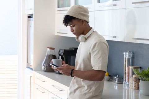 African american man checking phone holding coffee in modern minimalist kitchen